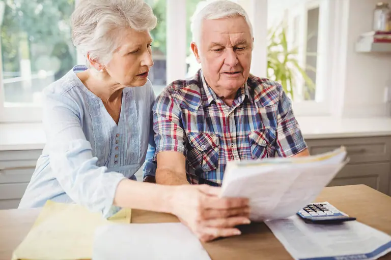 Older couple reviewing paperwork beside a calculator at a table