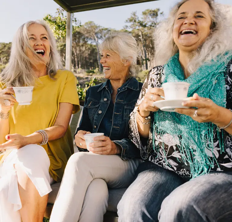 Three older women talking over cups at an outdoor table