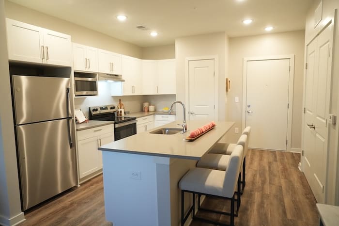 Kitchen in a one-bedroom apartment at Park Place by Highlands with white cabinetry, stainless steel appliances and a quartz island with bar stools